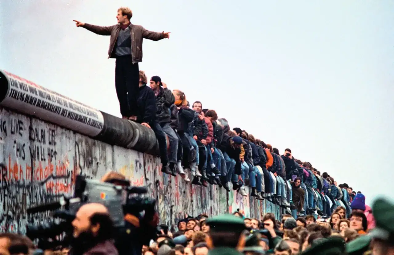 Radość i wolność po upadku Muru Berlińskiego. Ludzie siedzą na szczycie, świętując historyczny moment.