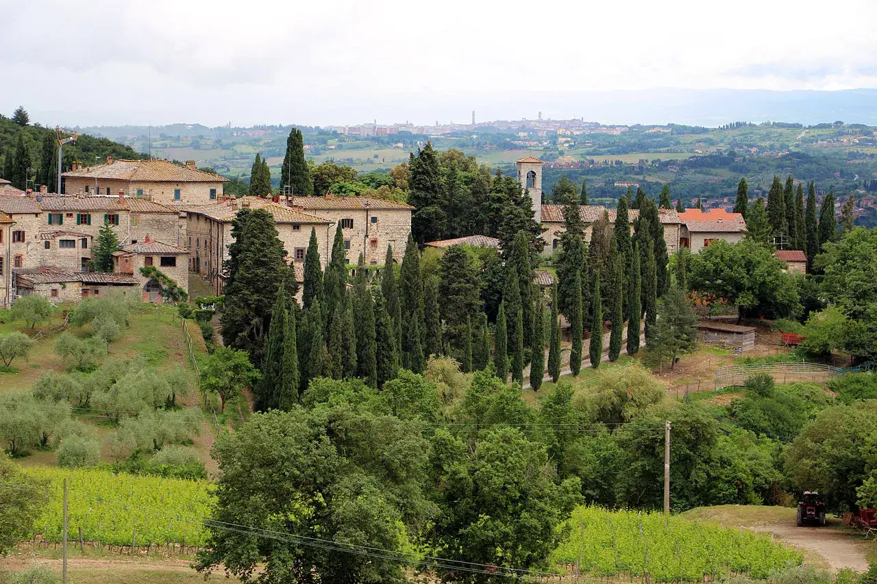 Paesaggio toscano con borgo in pietra, cipressi e vigneti. Una **strada chiantigiana mappa** ideale per un viaggio tra colline verdi.