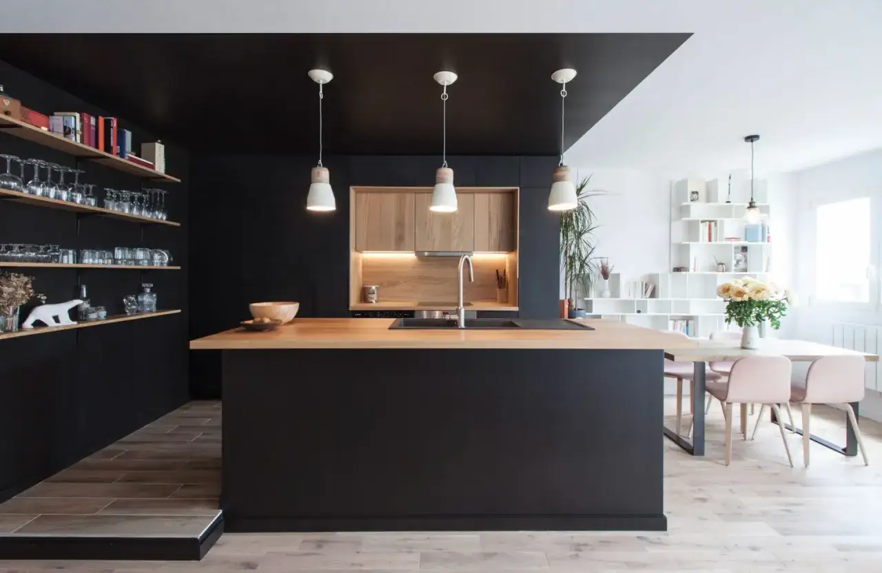 Cuisine moderne avec &icirc;lot central en bois, armoires noires et carrelage marron fonc&eacute; au sol.