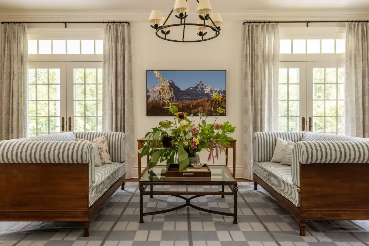 A cozy living room with two striped sofas, a floral arrangement, and a mountain landscape painting. Chris loves Julia's house!