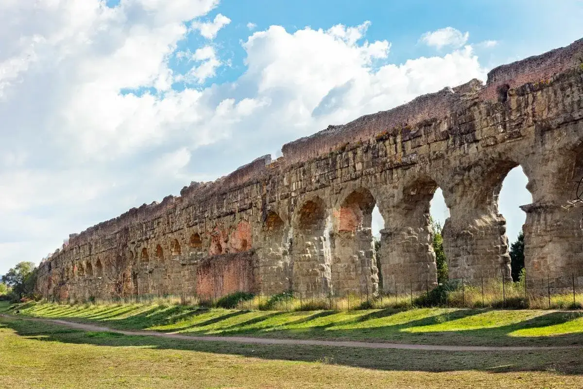 Vestiges de la voie appienne &agrave; Rome, un aqueduc antique aux arches imposantes se dresse sous un ciel bleu et nuageux.