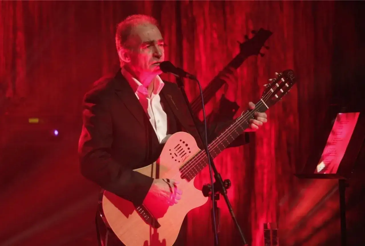 Seweryn Krajewski na scenie, grając na gitarze i śpiewając swoje piosenki. W tle basista.