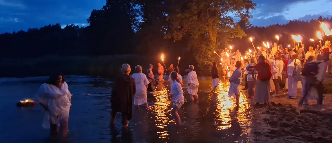 Nocne obrzędy nad wodą, ludzie z pochodniami szukają mitycznego kwiatu paproci.
