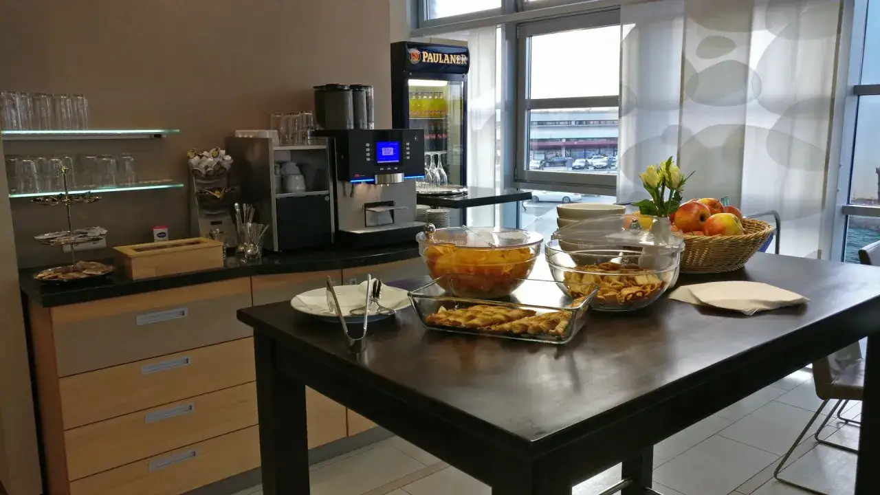 Snacks und Getränke in der **Priority Pass Lounge Berlin**. Obst, Gebäck und eine Kaffeemaschine stehen bereit.