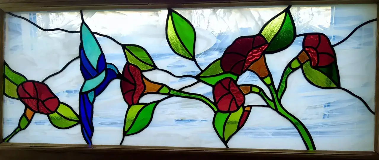Un vitrail aux couleurs vives représentant des fleurs rouges et des feuilles vertes, avec un oiseau bleu. Une œuvre d'art qui pourrait être le résultat d'un cours de vitrail.