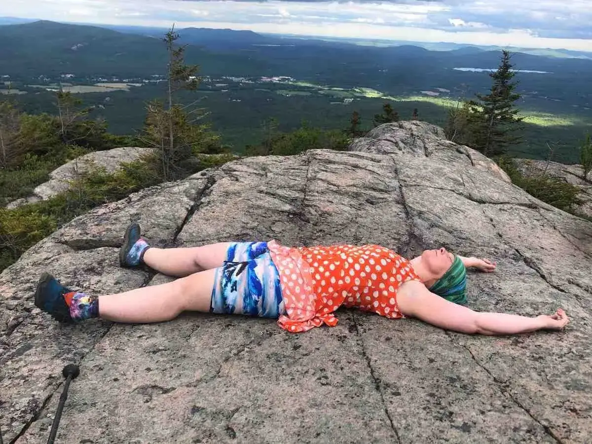 Donna si gode il panorama dall'alto, sdraiata su una roccia con un **gita outfit montagna estate** colorato.