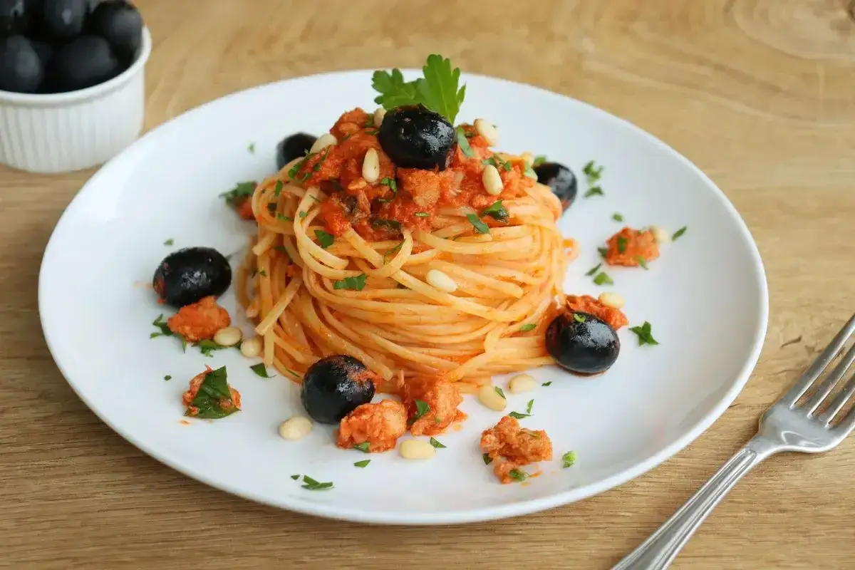 Spaghetti conditi con un sugo rosso, tonno fresco, olive nere, pinoli e prezzemolo. Un piatto invitante e saporito.