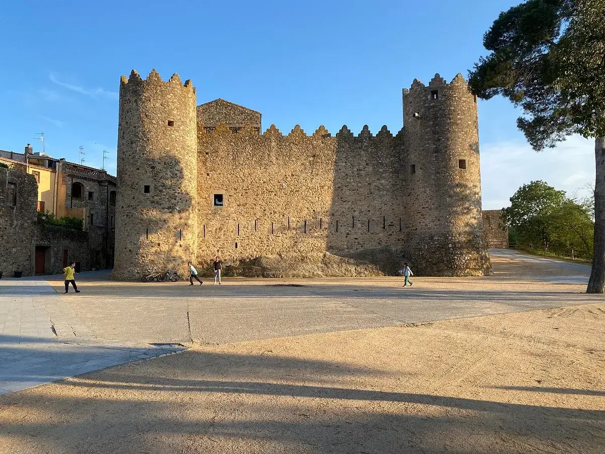 Alte Burgmauern in Calonge, Spanien, mit Kindern, die auf dem Platz spielen.