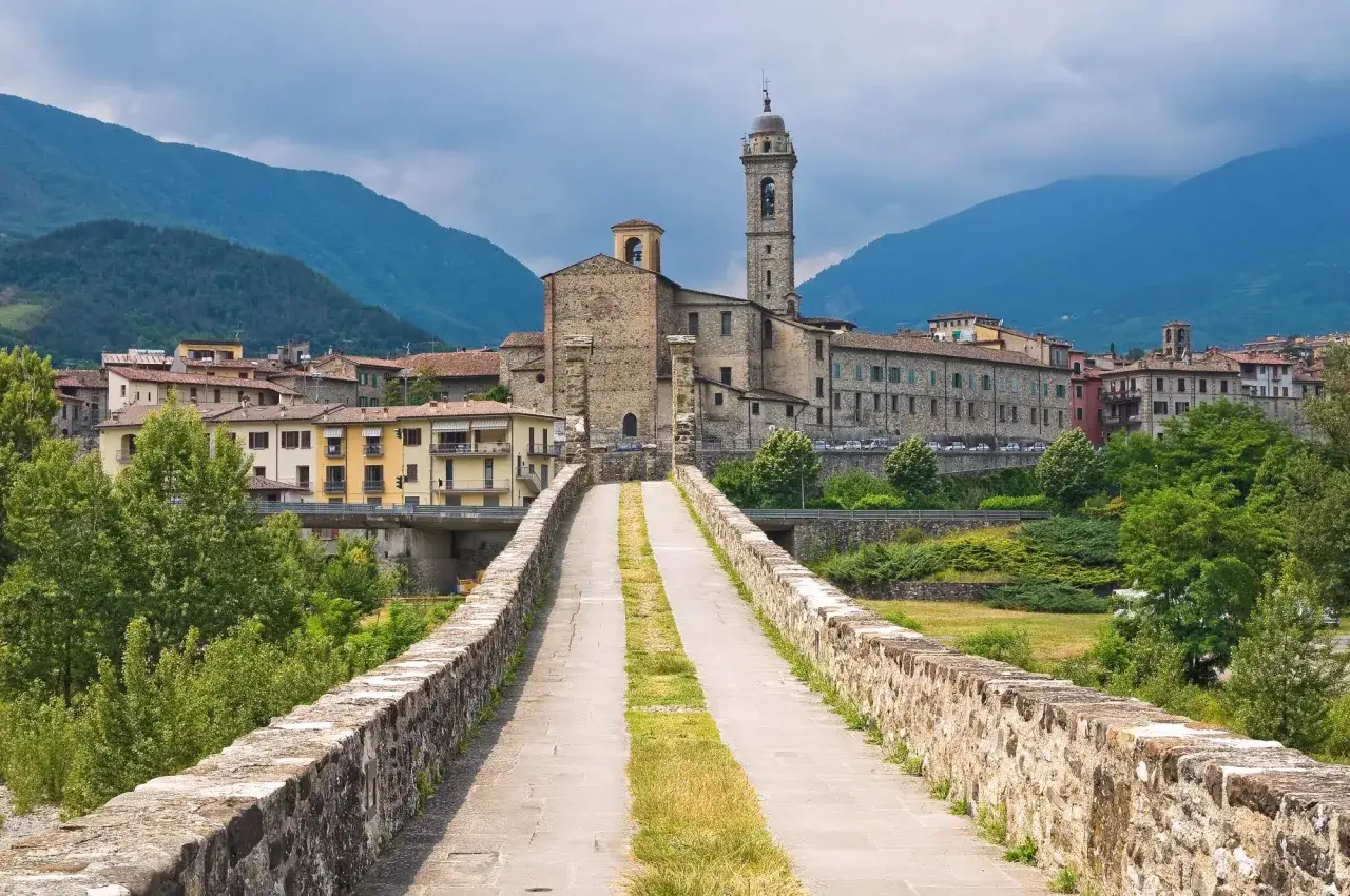 Ponte storico in pietra che conduce a un borgo italiano con campanile. Ideale per un trekking di 5 giorni in Italia.