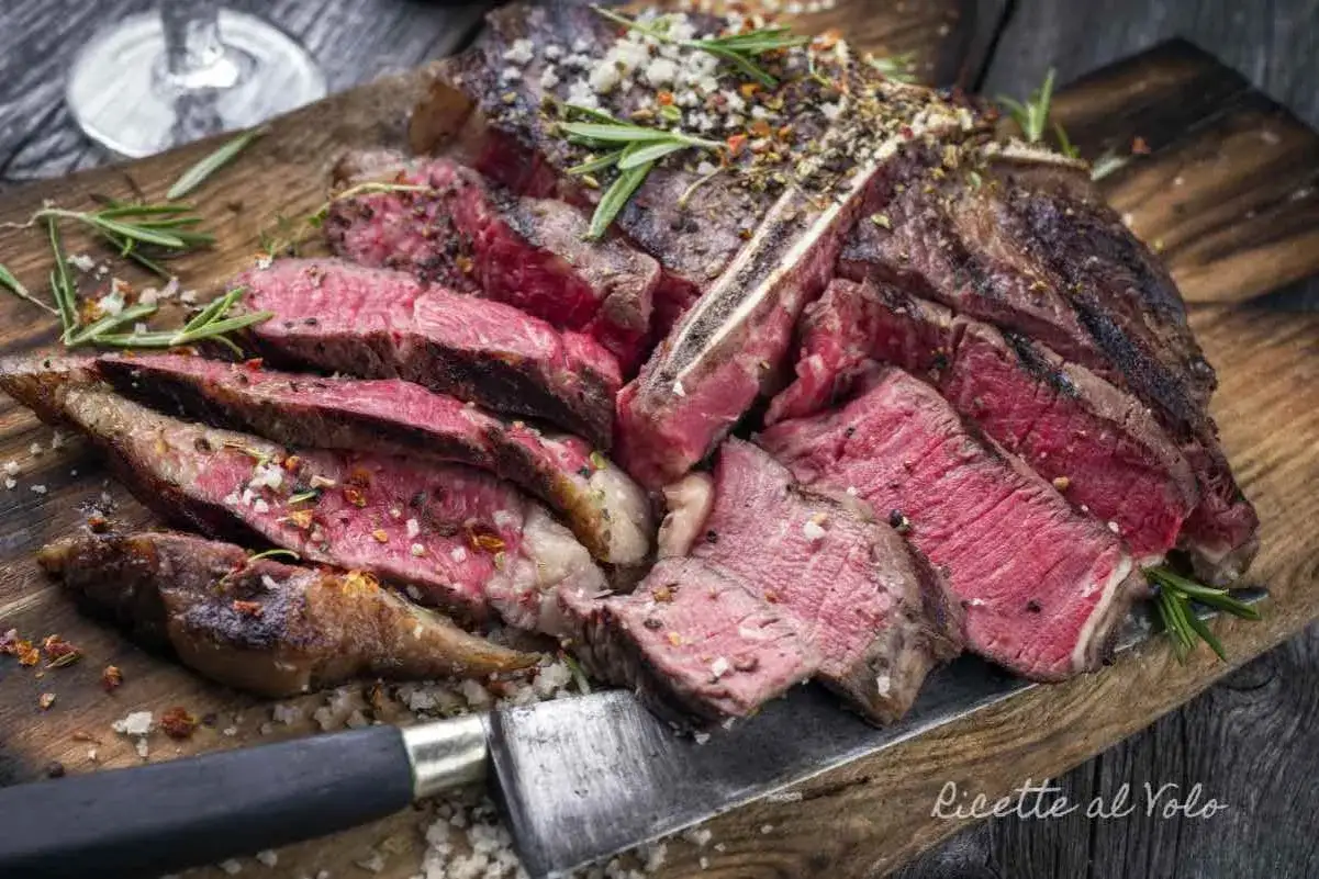 Un succulento bistec a la fiorentina, affettato e condito con sale grosso e rosmarino, pronto per essere gustato su un tagliere di legno.