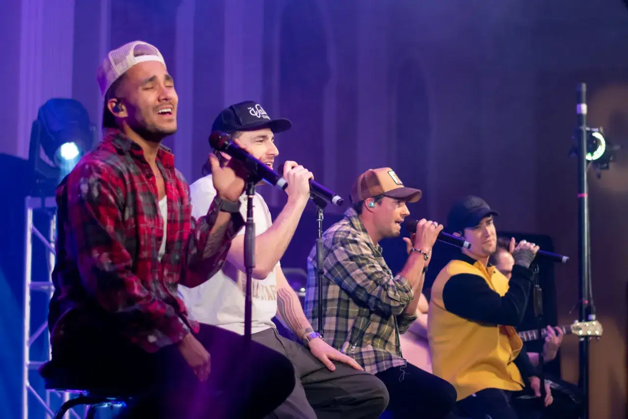Członkowie Big Time Rush śpiewają na scenie, każdy z mikrofonem.