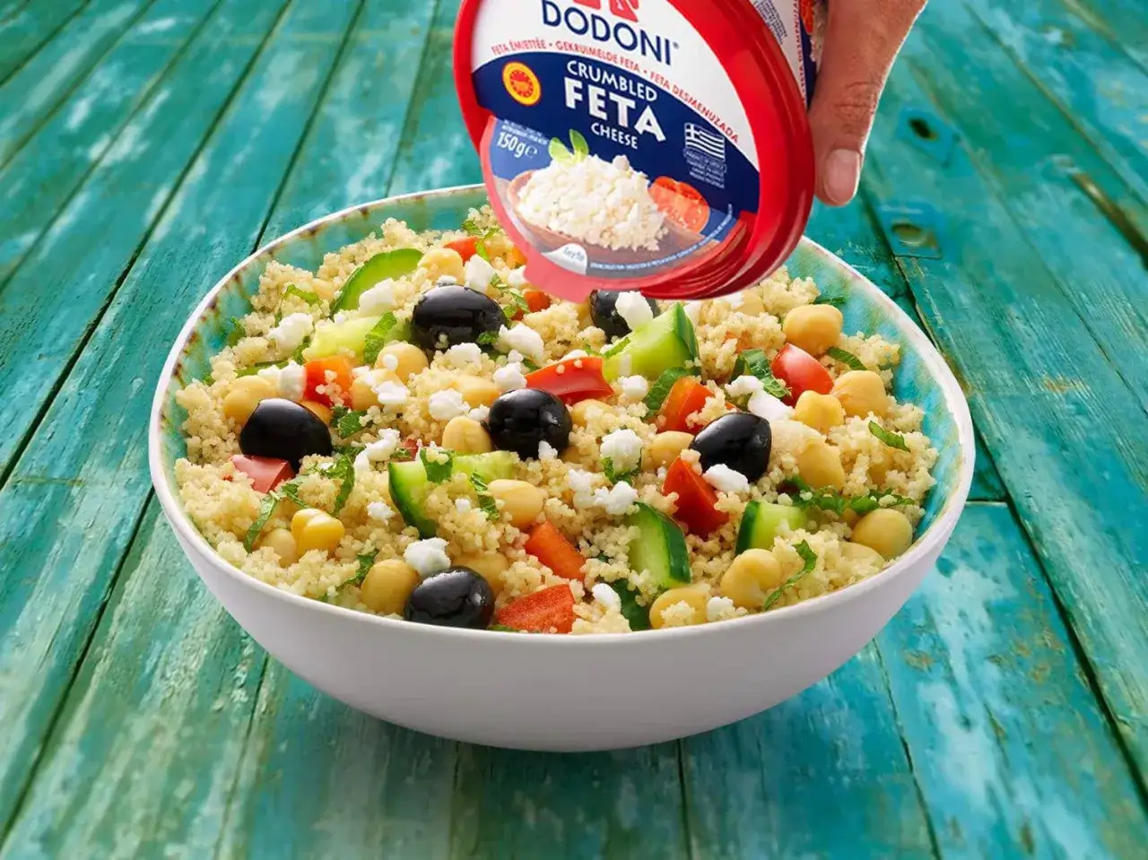 Ensalada cous cous con garbanzos, aceitunas, pepino y tomate, coronada con queso feta desmenuzado.