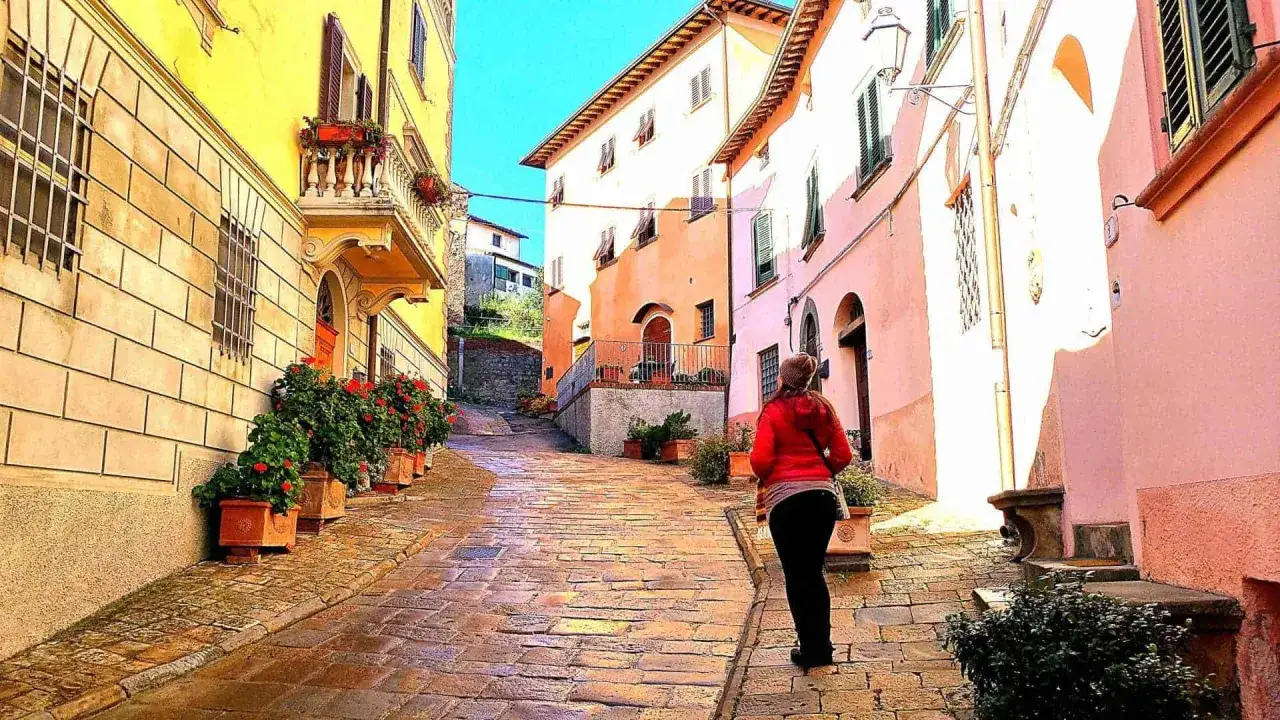 Una donna cammina su una strada acciottolata a Palaia, Pisa. Case colorate e fiori adornano il vicolo.