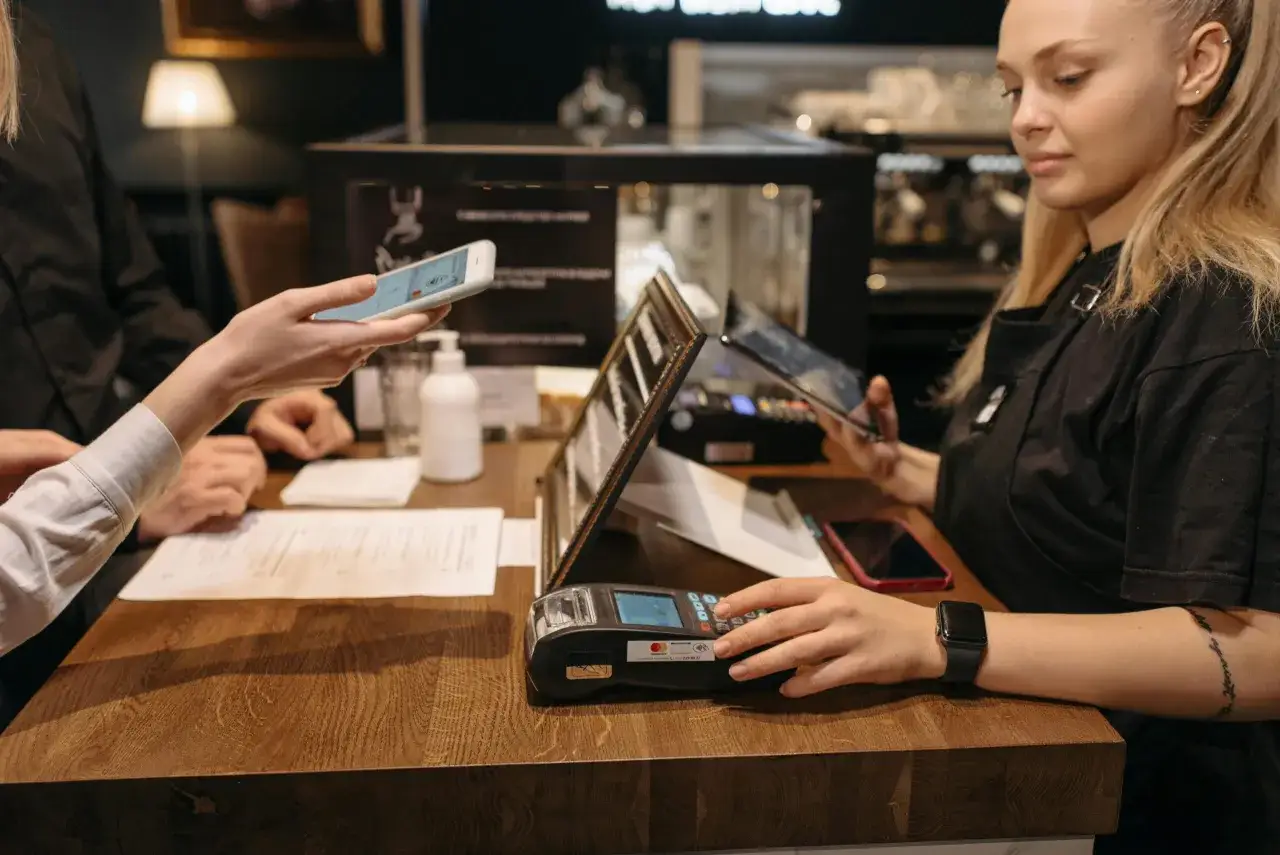 Eine Kundin hält ihr Handy über ein Terminal, um mit Handy zu bezahlen. Die Kassiererin beobachtet den Vorgang.