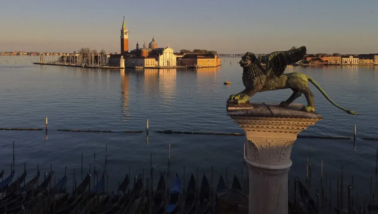 Leone alato veglia su Venezia, la Serenissima. Gondole ormeggiate e l'isola di San Giorgio Maggiore al tramonto.