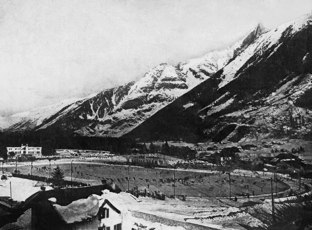 Widok na zimowe igrzyska olimpijskie 1924 w Chamonix. Śnieżne g&oacute;ry w tle, budynki i lodowisko.