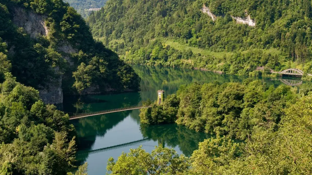 Un suggestivo ponte sospeso attraversa il lago di Corlo, incastonato tra montagne ricoperte di fitti boschi verdi.