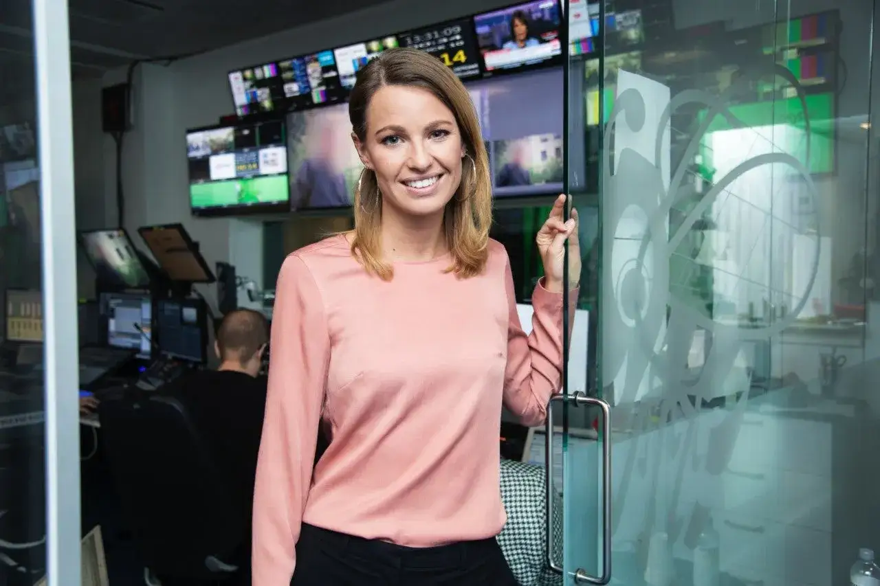 Jennie Pierrou ler vid en glasdörr i en kontrollrumsmiljö med många skärmar.