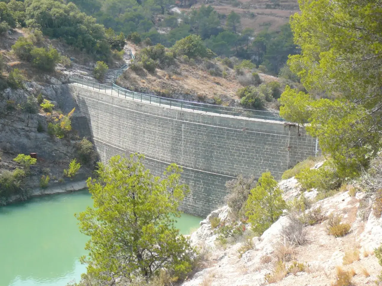 Barrage imposant retenant les eaux turquoise du lac Zola, entouré de végétation méditerranéenne.