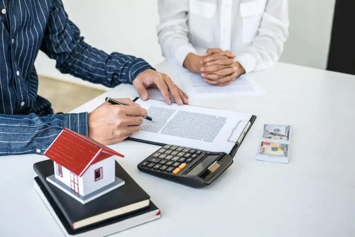 Firma di un accordo per una compropriet&agrave; con quote diverse. Sul tavolo, una casa modello, calcolatrice e denaro.