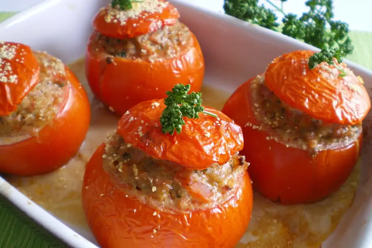 Quatre tomates farcies, garnies de persil frais, dans un plat blanc. Un délice à déguster !
