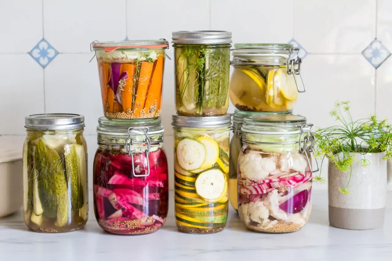 Bunte Gl&auml;ser mit fermentiertem Gem&uuml;se: Gurken, Karotten, Zucchini, Blumenkohl und rote Zwiebeln in Salzlake zum Fermentieren.