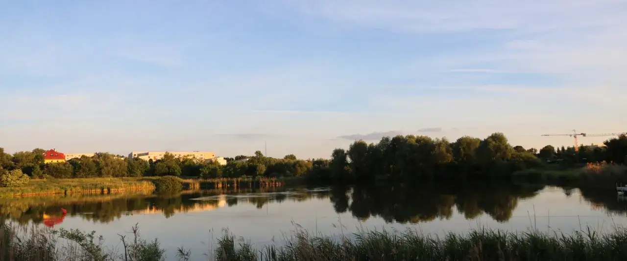 Spiegelglatte Wasserfl&auml;che am Wuhletal Wanderweg, reflektiert B&auml;ume und Geb&auml;ude. Ein rotes Haus sticht hervor.