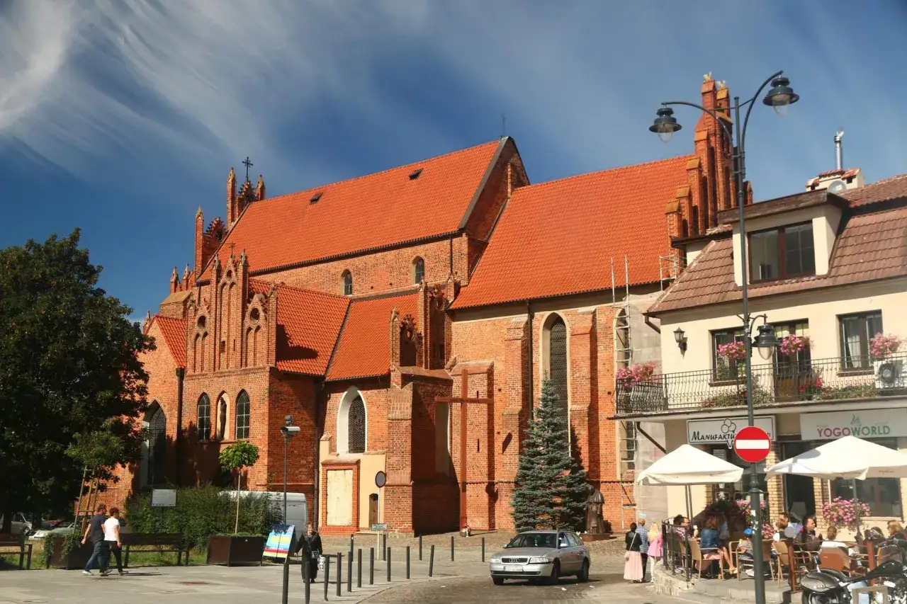 Gotycka ceglana bazylika w Tczewie, jedna z głównych atrakcji miasta, z widokiem na kawiarnię i ludzi spacerujących po placu.