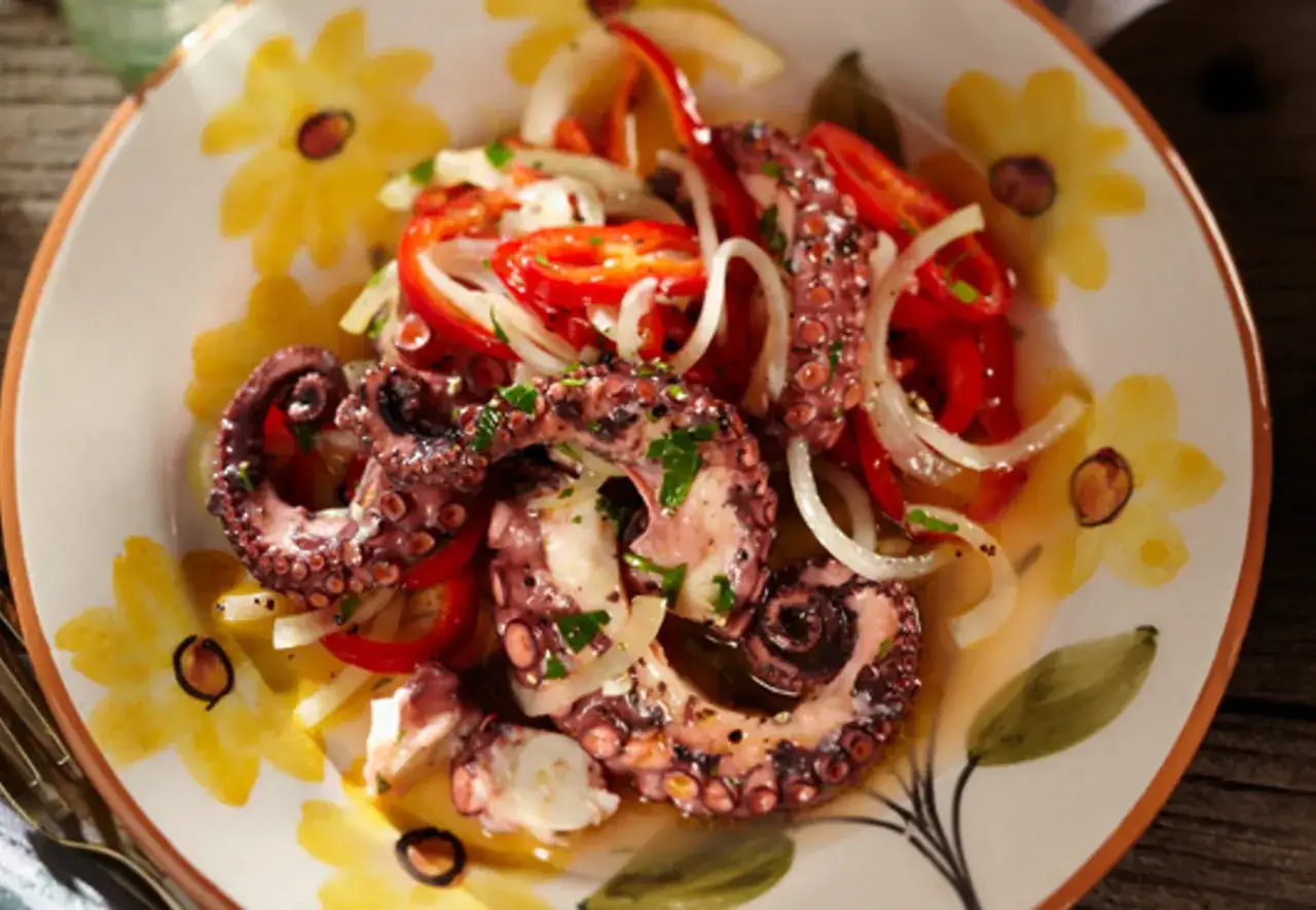Ein köstlicher Pulpo Salat mit Paprika und Zwiebeln, serviert auf einem Teller mit gelben Blumen.