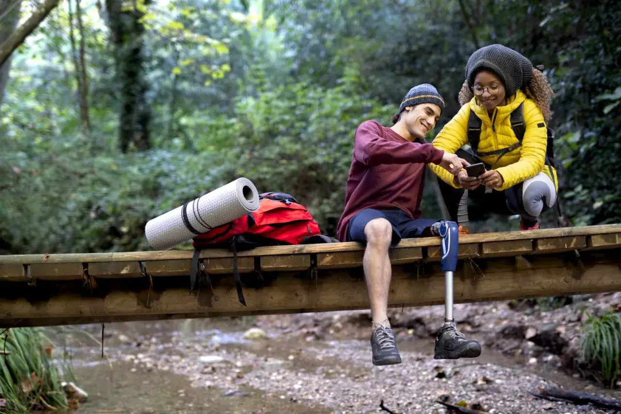 Zwei Rucksacktouristen mit Prothese auf einer Holzbr&uuml;cke im Wald, planen ihre weltreise backpacking.