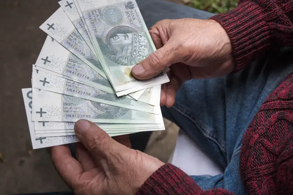 Ręce trzymają stos banknotów 100 zł. Czy Vivus wyplaca w sobotę? Pieniądze mogą pomóc w nagłych wydatkach.