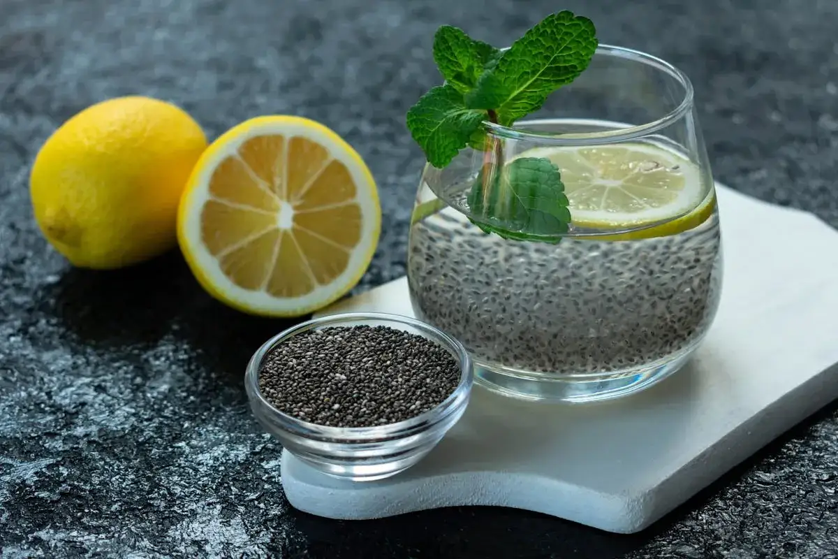 Verre d'eau de chia rafra&icirc;chissante avec des citrons et des feuilles de menthe. Une petite coupelle de graines de chia est &agrave; c&ocirc;t&eacute;.