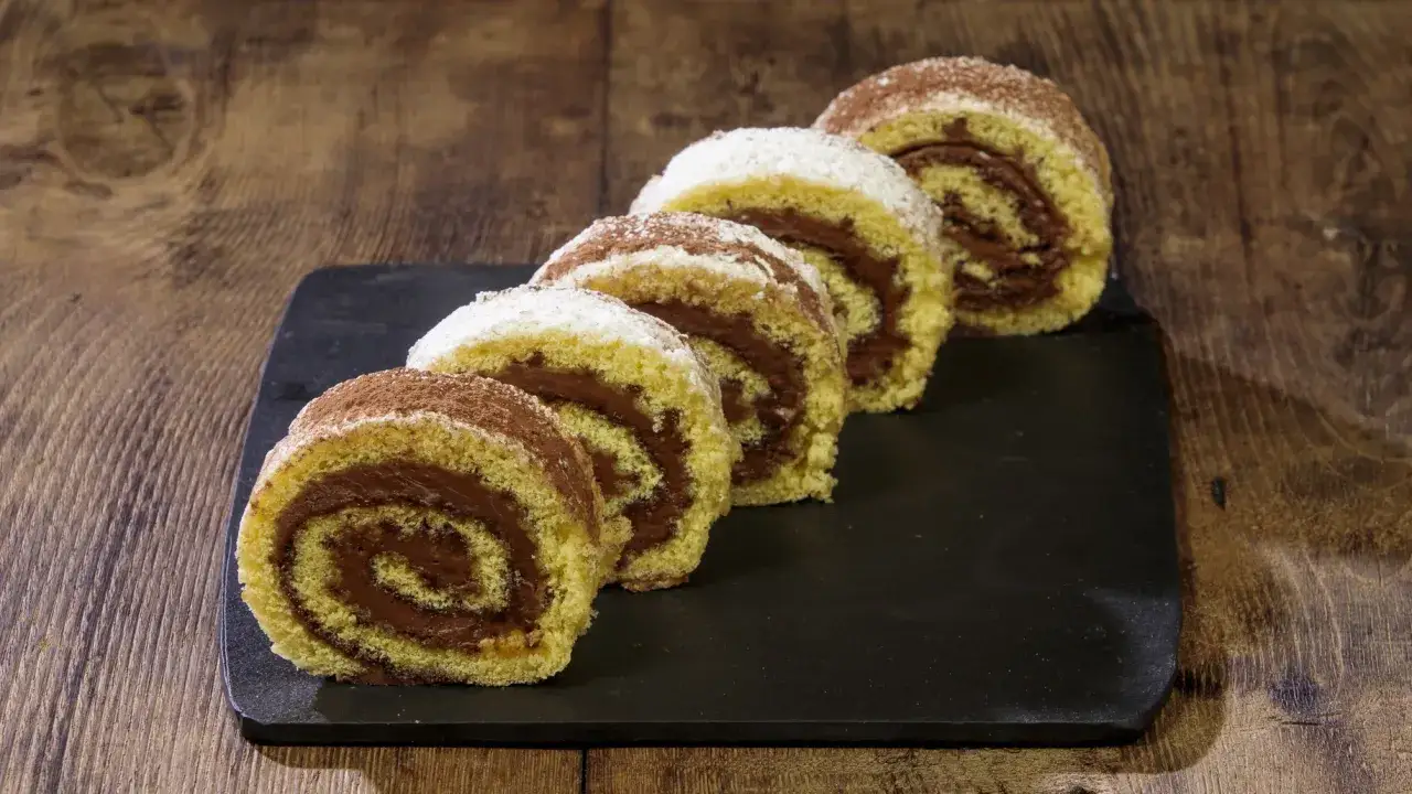 Fette di rotolo alla nutella cosparse di cacao e zucchero a velo, su una lavagna scura, pronte per essere gustate.