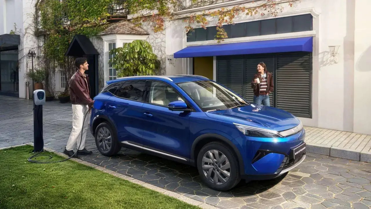 Un uomo carica la BYD ATTO 3, pronta per un lungo viaggio grazie alla sua eccellente autonomia. Una donna attende sorseggiando una bevanda.