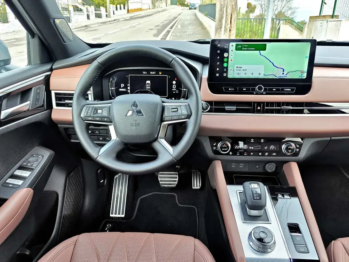 Wnętrze Mitsubishi Outlander PHEV z ekranem nawigacji i cyfrowymi zegarami. Skórzana tapicerka i nowoczesne detale.