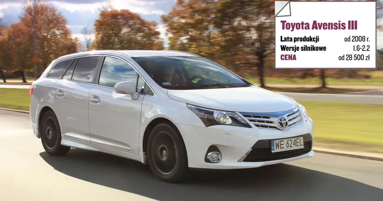Biała Toyota Avensis 2.0 D4D kombi w ruchu, z widocznym panelem informacyjnym o modelu.