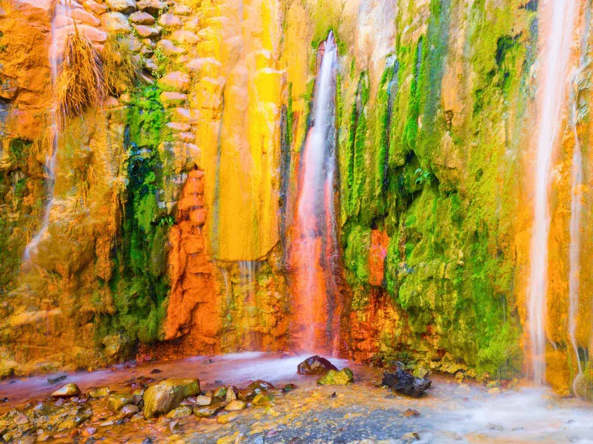 Una cascada de colores la palma, con rocas cubiertas de musgo verde vibrante y vetas anaranjadas y amarillas, crea un espectáculo natural.