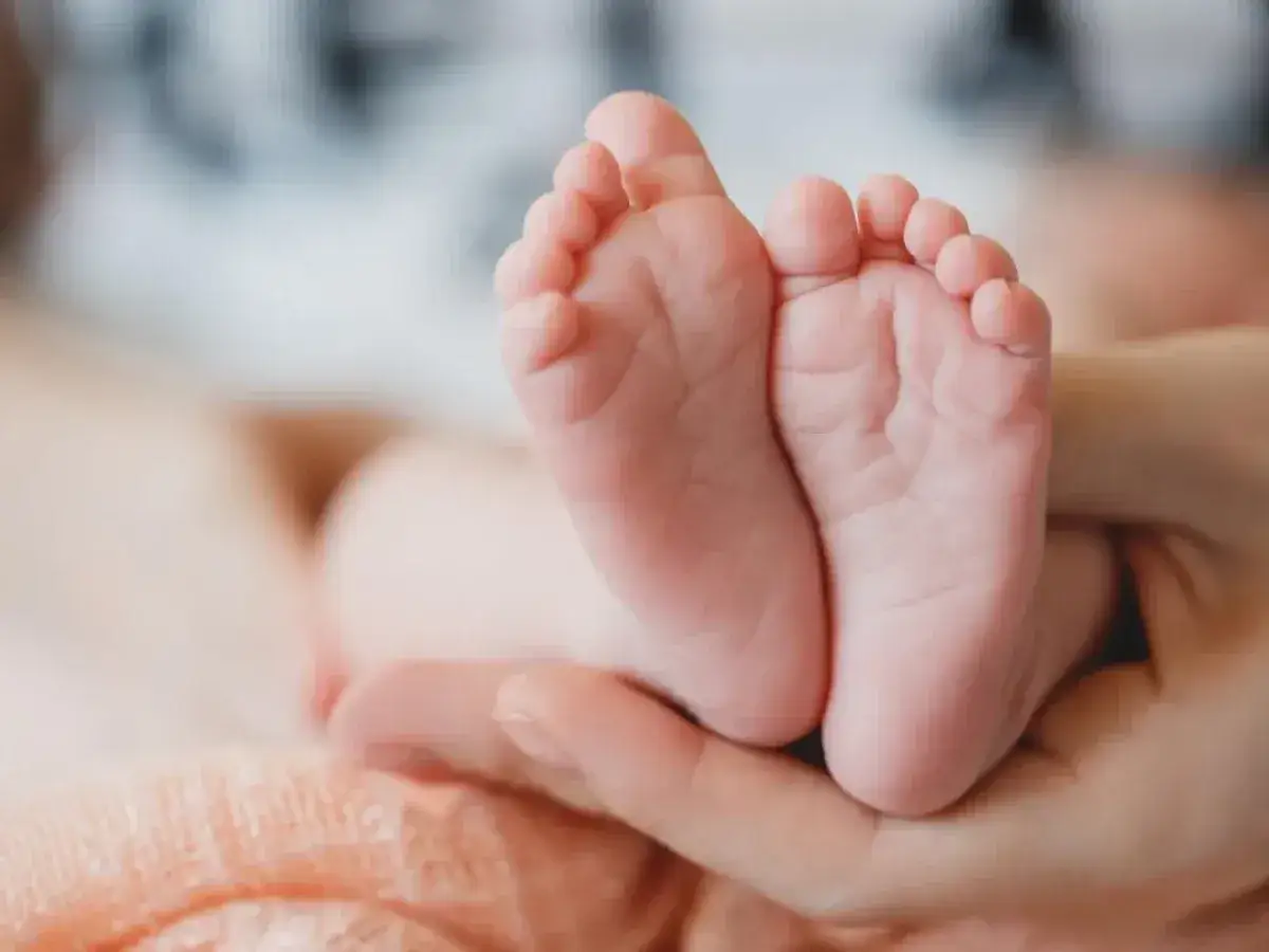 Manos adultas sostienen los peque&ntilde;os pies de un beb&eacute;. A mi beb&eacute; le sudan los pies, pero son tan adorables.
