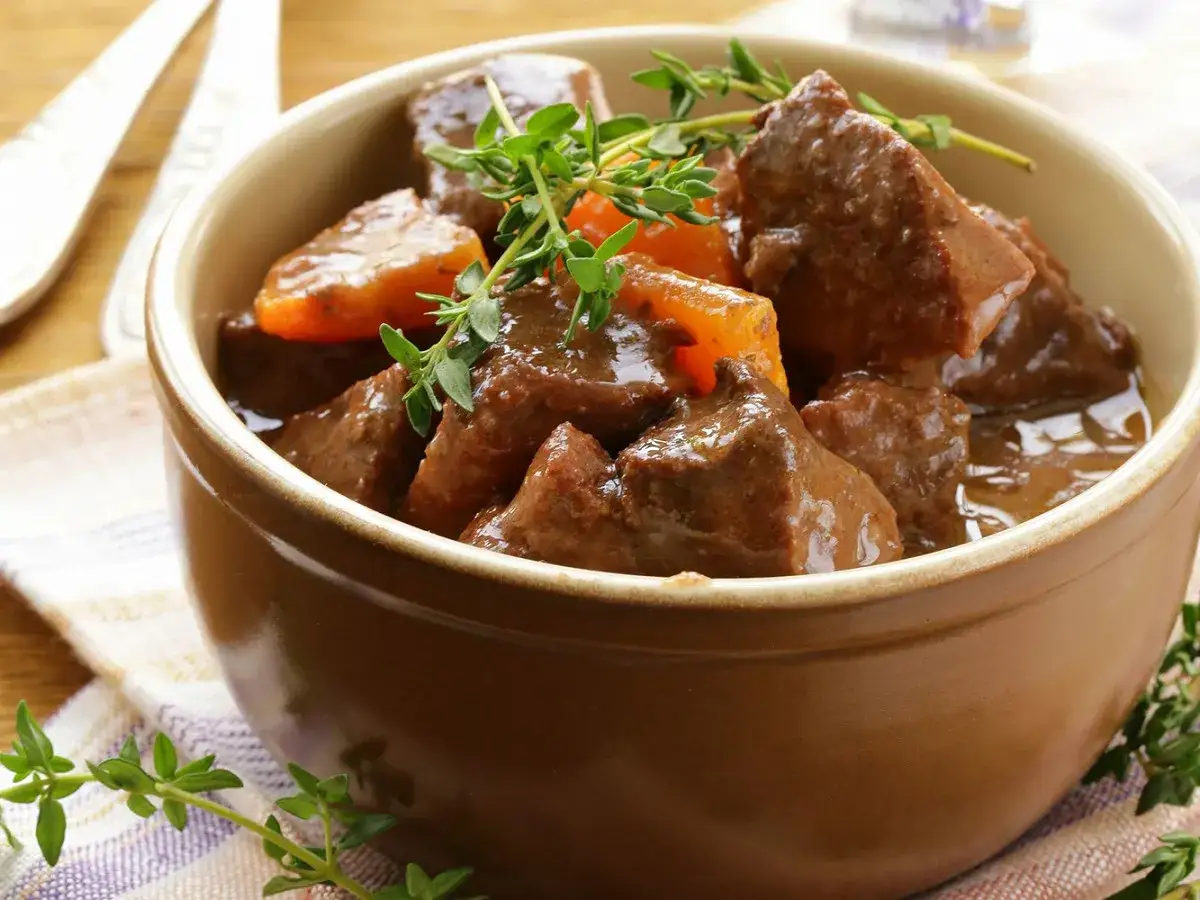 Un plat réconfortant de boeuf carottes mijoté, garni de thym frais, servi dans un bol en terre cuite.
