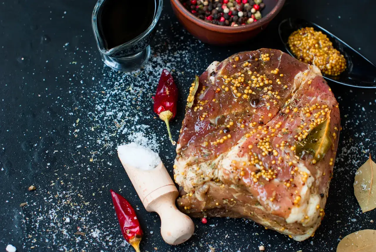 Karkówka na grillu elektrycznym w marynacie z musztardy i ziół, obok papryczki chili, soli i pieprzu.