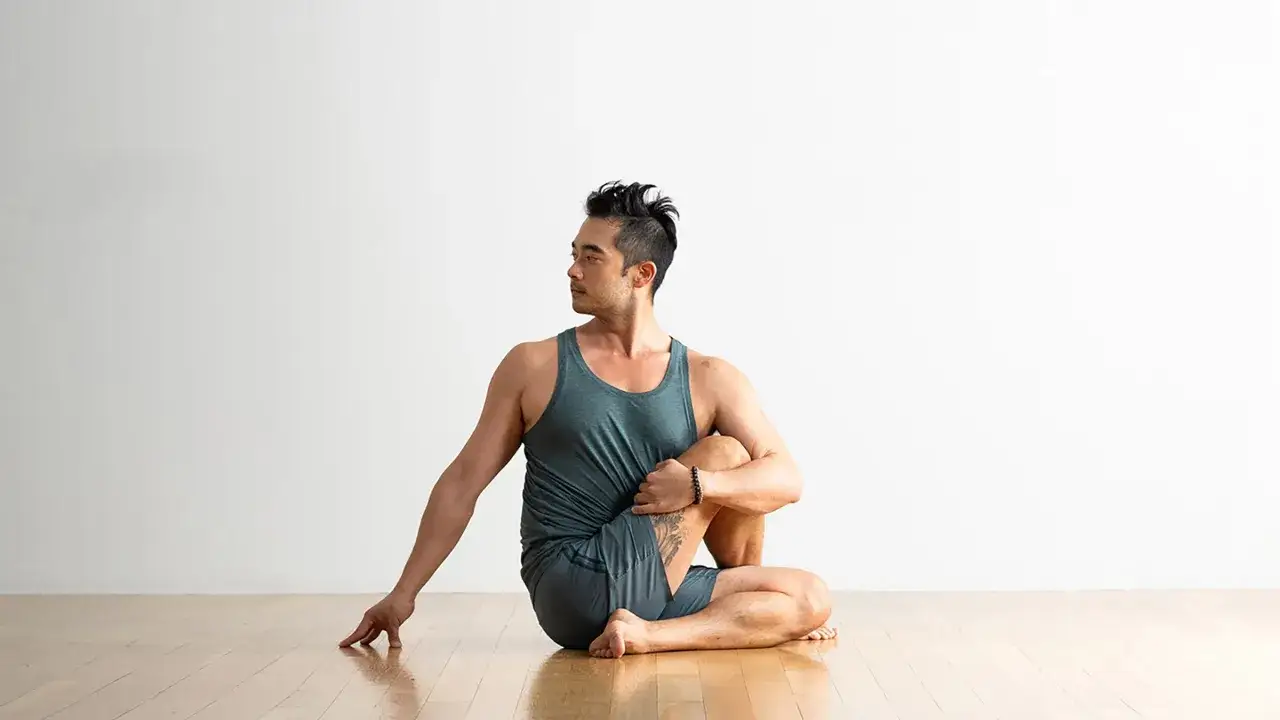 Hombre asiático en la postura de yoga ardha matsyendrasana, girando el torso.