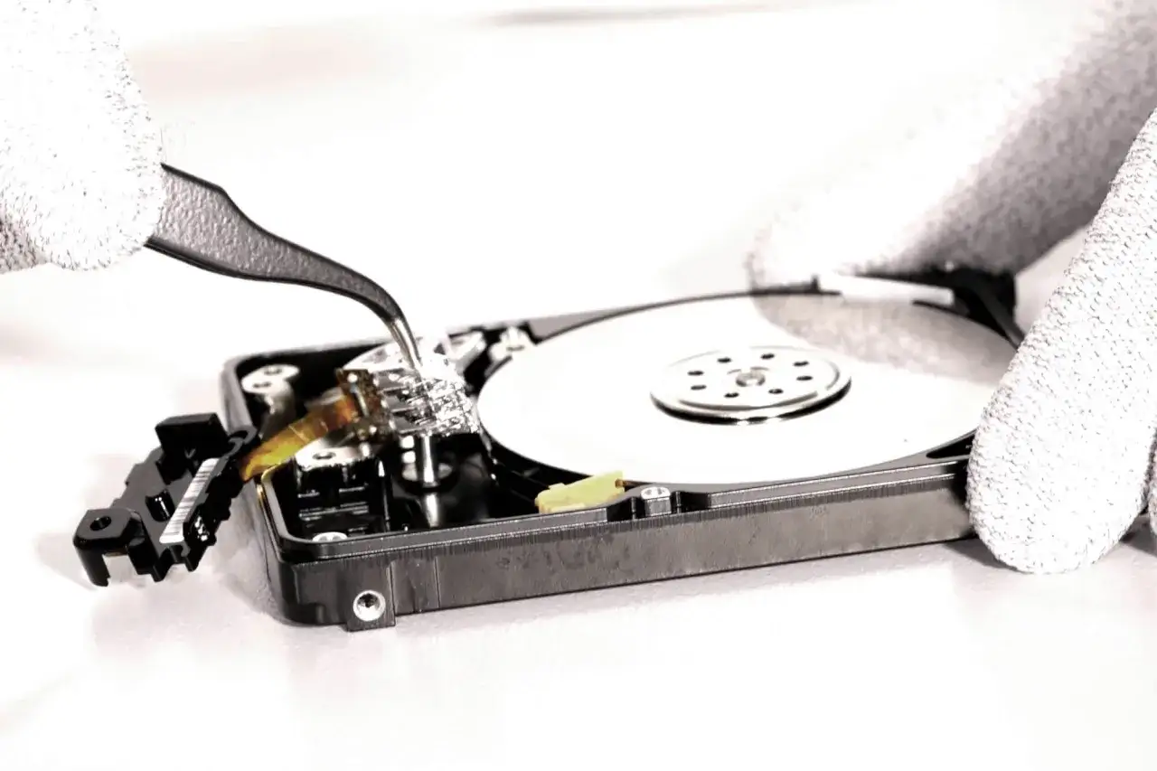 Hände mit Handschuhen reparieren eine Festplatte. Ein Werkzeug greift nach einem Bauteil, möglicherweise wegen eines smart hard disk error.