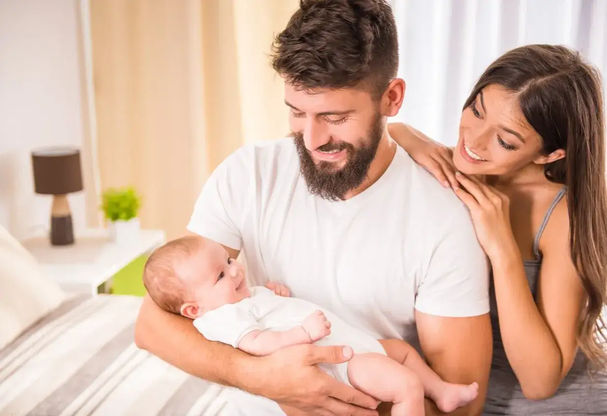 Szczęśliwi rodzice patrzą na swoje dziecko, kt&oacute;re świadomie się uśmiecha.