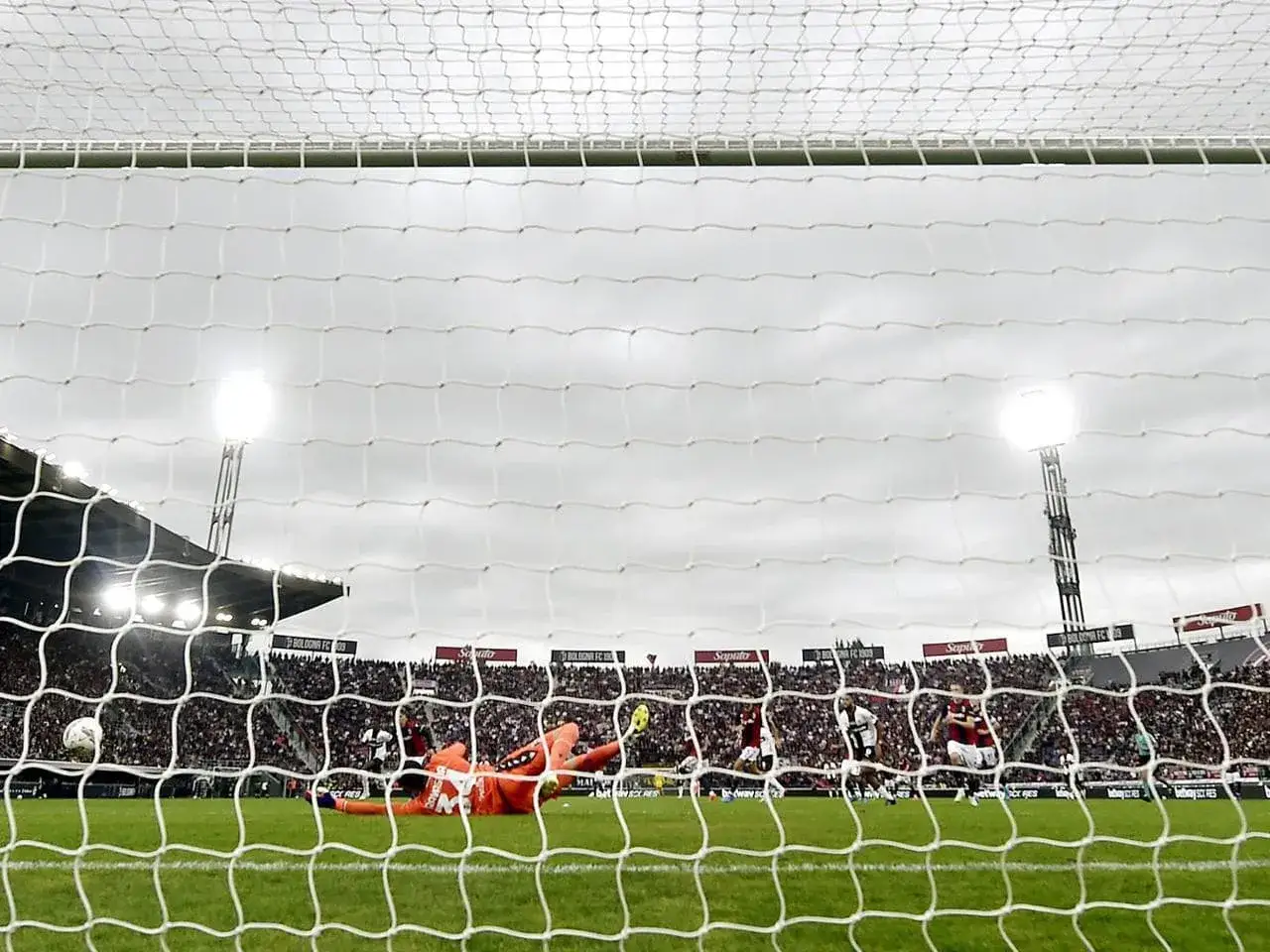 Bramkarz w akcji ratuje bramkę w meczu Bologna &ndash; Parma. Tłumy kibic&oacute;w na stadionie.