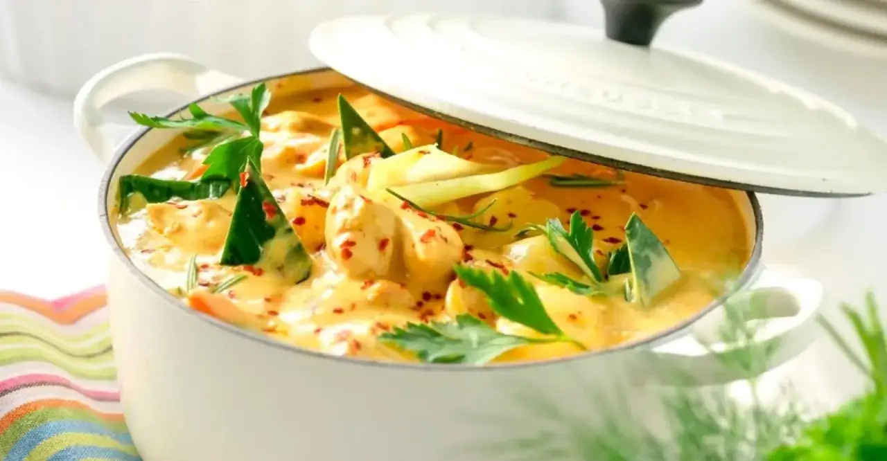 A creamy Thai chicken curry in a white pot, garnished with fresh herbs and chili flakes.