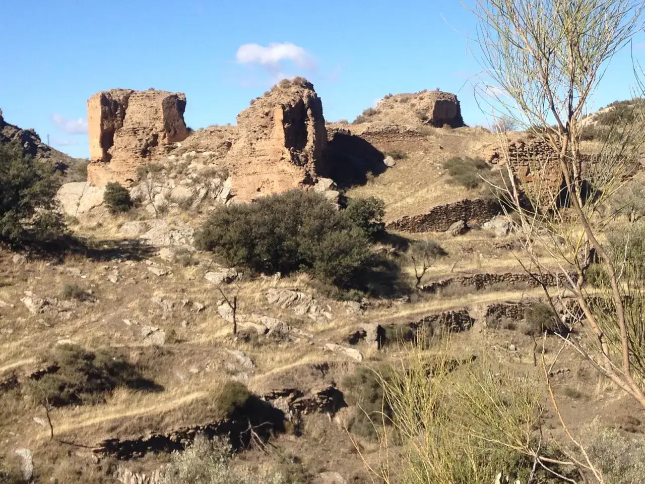 Ruinas de la jirola abrucena, un antiguo asentamiento en una colina rocosa, con vegetaci&oacute;n seca y un cielo azul.