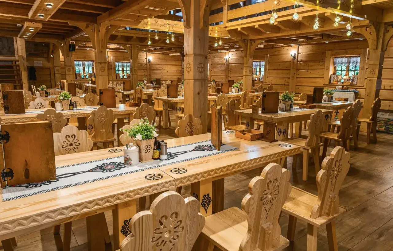 Drewniana borowa chata zaprasza. Na stołach ozdobne bieżniki, kwiaty. Cennik i menu gotowe do podania.