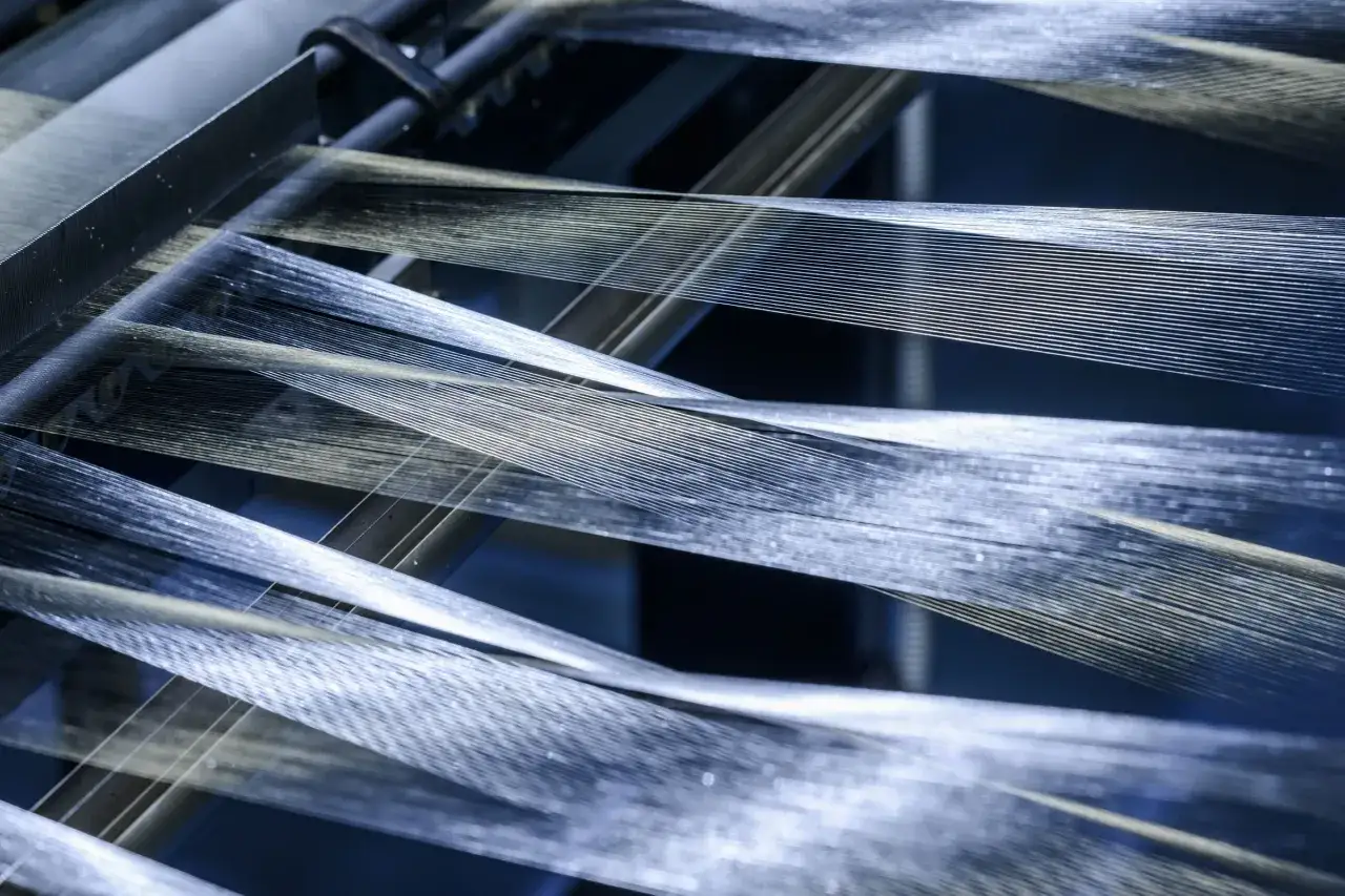 Fils brillants de fibre synth&eacute;tique tendus sur une machine, cr&eacute;ant un effet visuel captivant.