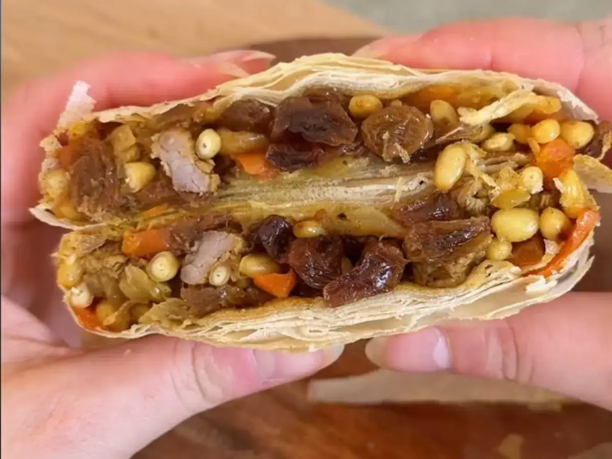 Une pastilla agneau coupée en deux, révélant sa garniture généreuse de viande, raisins secs, pignons et carottes. Un délice croustillant et sucré-salé.