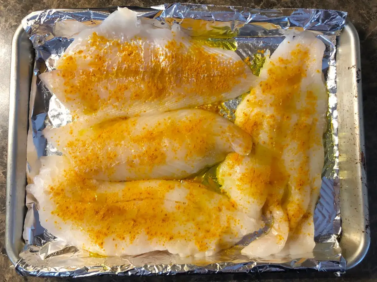 Filetes de merluza cruda sazonados con especias amarillas sobre papel de aluminio en una bandeja. &iexcl;Los perros pueden comer merluza!